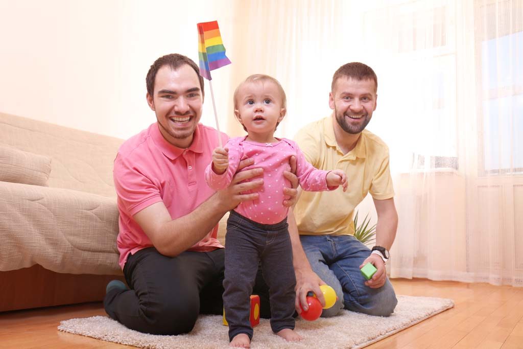 Two same-sex parents with their child, holding a rainbow pride flag.